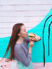 Smiling girl with a burger against a bright wall. Photo for advertising