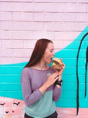Smiling girl bites a burger against a bright wall. Photo for advertising