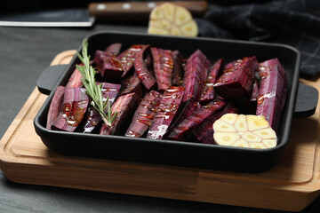 Black raw cut carrot with garlic and rosemary in baking dish on black table, closeup