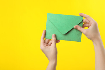 Woman holding green paper envelope on yellow background, closeup