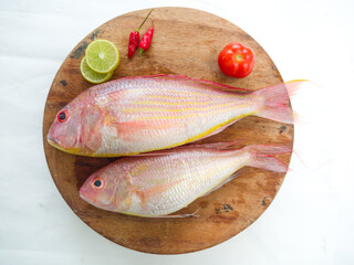 Fresh and ready to cook raw pink Perch fish with ingredients like lemon,chilli and tomatoes on a wooden pad,white background, selective focus.