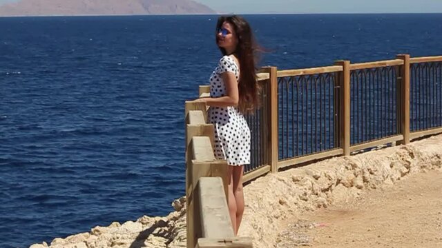 A lovely young girl in a white dress with polka dots posing against the backdrop of the sea and the island in Egypt.