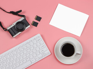 flat lay of camera, memory card, computer keyboard, coffee cup and blank photo paper on pink background.
