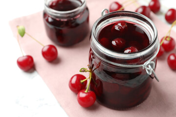 Jars of pickled cherries and fresh fruits on table, closeup