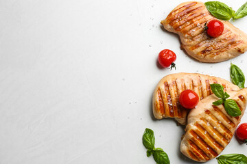 Tasty grilled chicken fillets with cherry tomatoes and green basil on light grey table, flat lay....