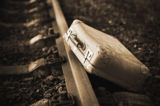 Next to the railway is an old worn-out retro suitcase, forgotten during the trip. 20th century. Immigration. Sepia.