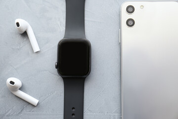 Stylish smart watch, phone and earphones on grey stone table, flat lay