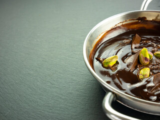 Melted dark chocolate with pistachios. Copy space and recipe template. Small pan with cocoa mousse. Tempered chocolate. Cooking sweets at home. Prepare a dessert. Cacao hot cream.