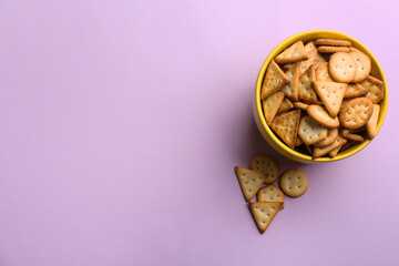 Delicious crackers in bowl on violet background, flat lay. Space for text