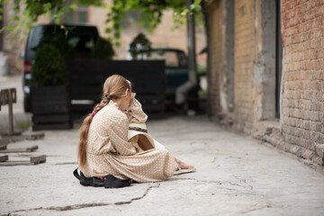 A beautiful long-haired girl sits on the asphalt in the street and holds her head. Headache and bad mood
