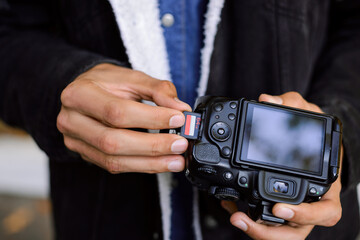 Close-up picture of DSLR camera in the hands of a man, putting flash card SD of 64 GB in it.