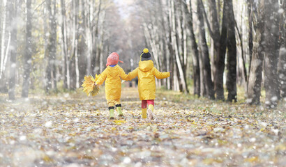 Fototapeta premium Toddlers on a walk in the autumn park. First frost and the first snow in the autumn forest. Children play in the park with snow and leaves.