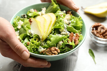 Woman holding tasty salad with pear slices at table, closeup