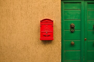 Red mailbox hanging on the wall of a house with a green door (