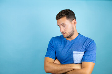 Young handsome man wearing blue casual t-shirt over isolated blue background skeptic and nervous, disapproving expression on face with crossed arms