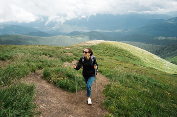 A young woman with hiking sticks climbs to the top of the mountain in a hiking wear and enjoying with amazing landscapes of a mountains around her