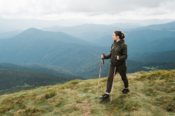 A young woman with hiking sticks walks on the mountains in a hiking wear and enjoying with amazing landscapes of a mountains