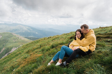 Naklejka na ściany i meble Love in the mountains. A loving couple of Caucasian ethnicity hugging while sitting on the top of the mountain, enjoying each other, the landscape and harmony