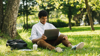 Smiling student looking on laptop screen in park