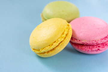 Almond cookies on blue background with copy space. Pink, yellow and green macaroons close up