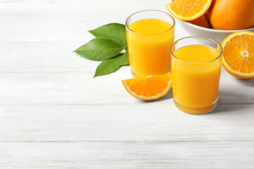 Glasses of orange juice and fresh fruits on white wooden table. Space for text