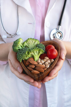 Healthy food for heart, diet concept. Doctor holding bowl with vegetables, almond nuts and chickpea. Close up, vertical