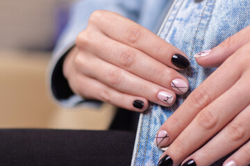 
Close up view of beautiful female hands with fashion manicure nails, nude and black gel polish, on jeans background