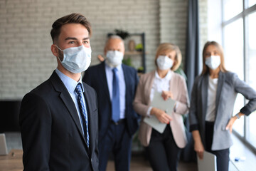 Businessman in medical mask with colleagues in the background in office.
