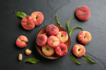 Fresh ripe donut peaches with leaves on dark table, flat lay