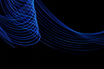 Long exposure photograph of neon blue colour in an abstract swirl, parallel lines pattern against a black background. Light painting photography.