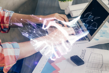 Handshake hologram drawing with businessman working on computer on background. Double exposure.