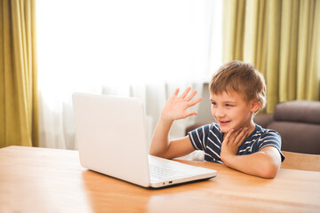 portrait of smiling school kid waving hand, making video call or recording video vlog to webcam at home. 
