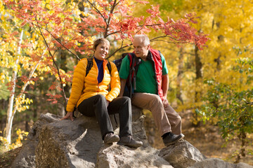 Senior couple  with backpack on a walk in an autumn nature. hyper-local travel,  family outing, getaway, natural environment
