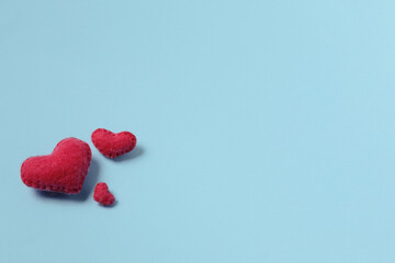 Three red felt hand-made hearts of different shapes are on a blue paper background. The concept of the family. A symbol of love happiness and devotion. Copy space.