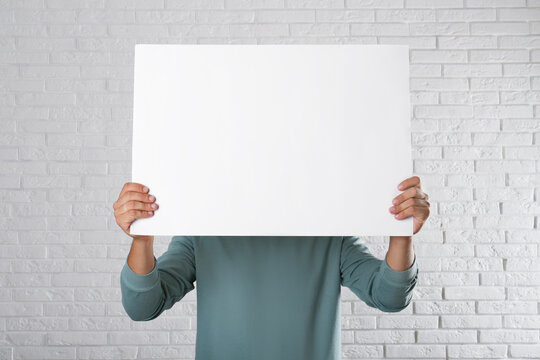 Man holding blank poster near white brick wall. Mockup for design