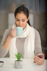 woman in the home drinking coffee and looking at smartphone