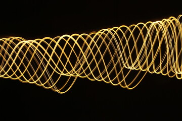 Long exposure photograph of neon gold colour in an abstract swirl, parallel lines pattern against a black background. Light painting photography.