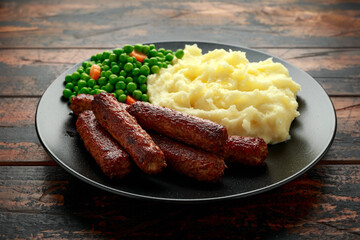 Vegetarian vegan sausages with mashed potato and green peas in black plate