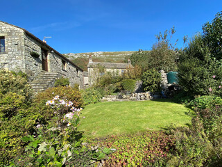 Fototapeta na wymiar Country cottages, with stone walls, a green lawn, wild plants, and fells in the distance, on a hot summers day in, Hawkswick, Skipton, UK