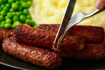 Vegetarian vegan sausages with mashed potato and green peas in black plate