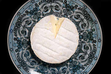 Coulommiers cheese in a decorated blue plate and black background	