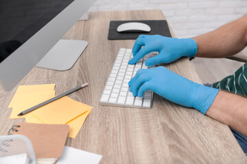 Office employee in latex gloves working with computer at wooden table, closeup