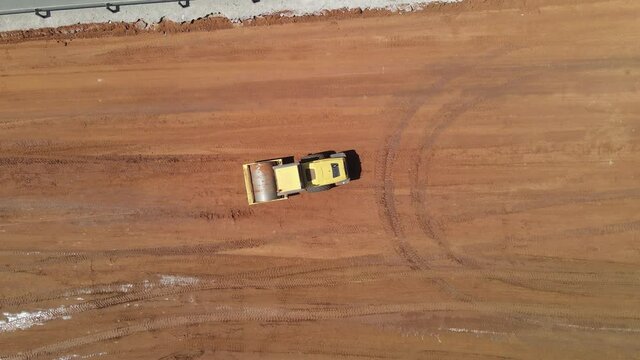 Aerial view of heavy machinery a road roll working in construction site on a new high way, heavy equipment top down footage
