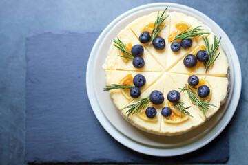 Homemade cheesecake with fresh blueberry and candied lemon on black stone background.