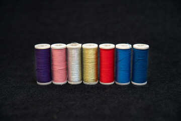 Spools of colorful sewing threads on a dark background	