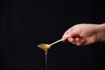 Spoon of liquid honey on black background