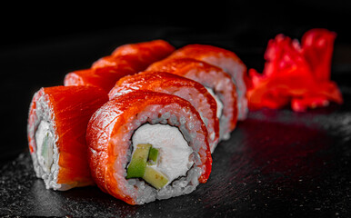 sushi roll with salmon, avocado, cream cheese in plate on black wooden table background