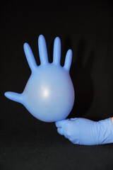 Blue gloved hand, holding another surgical glove inflated with air