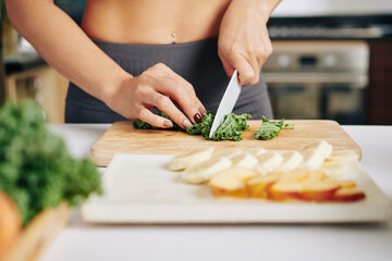 Close-up image of fit young woman cutting kale leaves and making smoothie