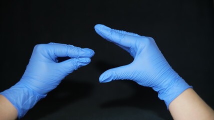 Two hands dressed in blue surgical gloves, mimicking a puppet that opens its mouth to eat the...